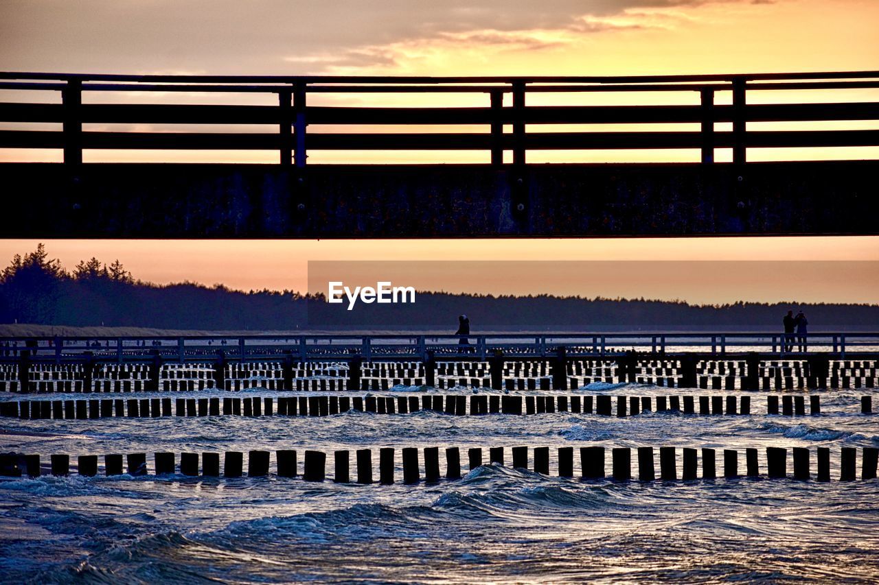 reflection, pier, water, sky, sunset, nature, architecture, wave, evening, sea, built structure, bridge, horizon, dusk, no people, railing, cloud, beauty in nature, ocean, beach, scenics - nature, outdoors, land, travel destinations, in a row, silhouette, environment