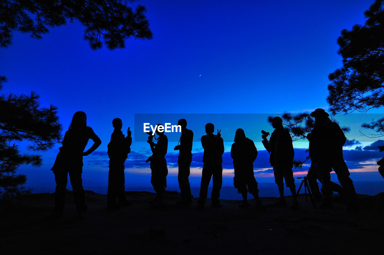 Silhouette people standing on field against blue sky