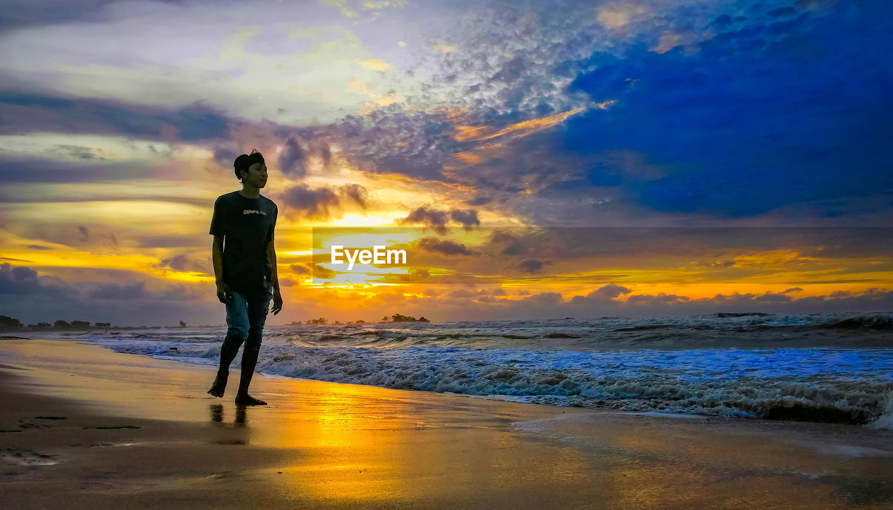 REAR VIEW OF MAN STANDING ON BEACH