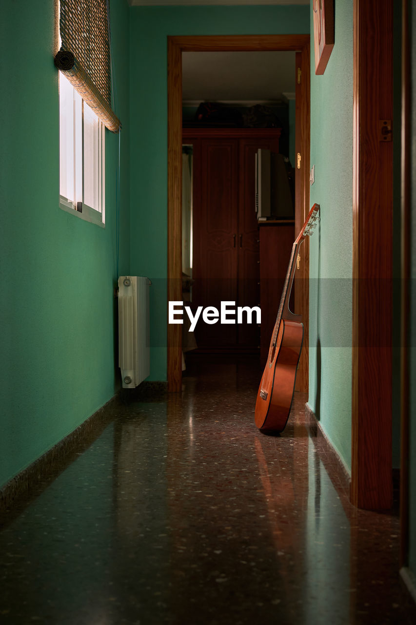 A guitar is leaning against the wall of a hallway in a house