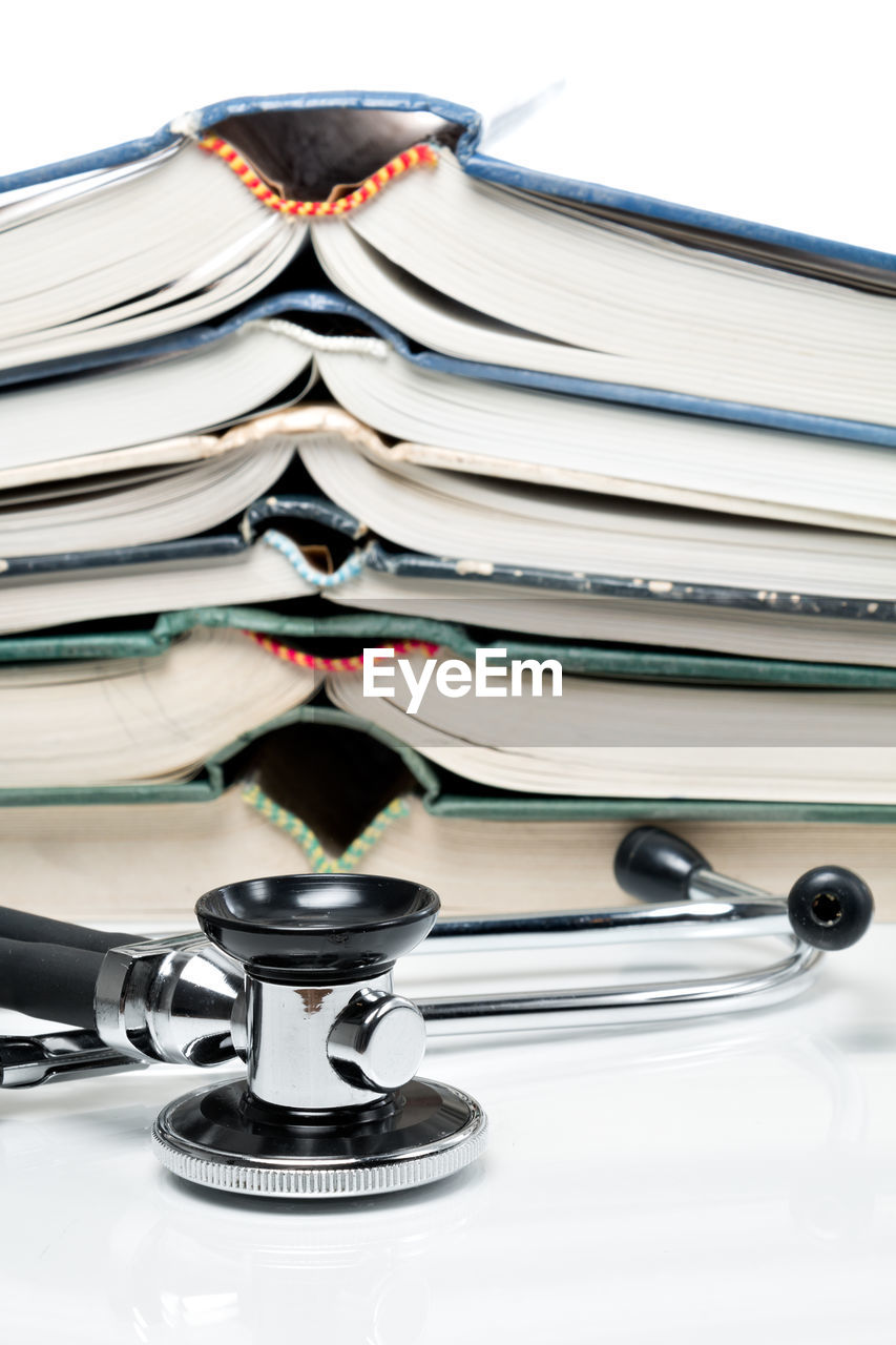 Close-up of books stacked by stethoscope against white background