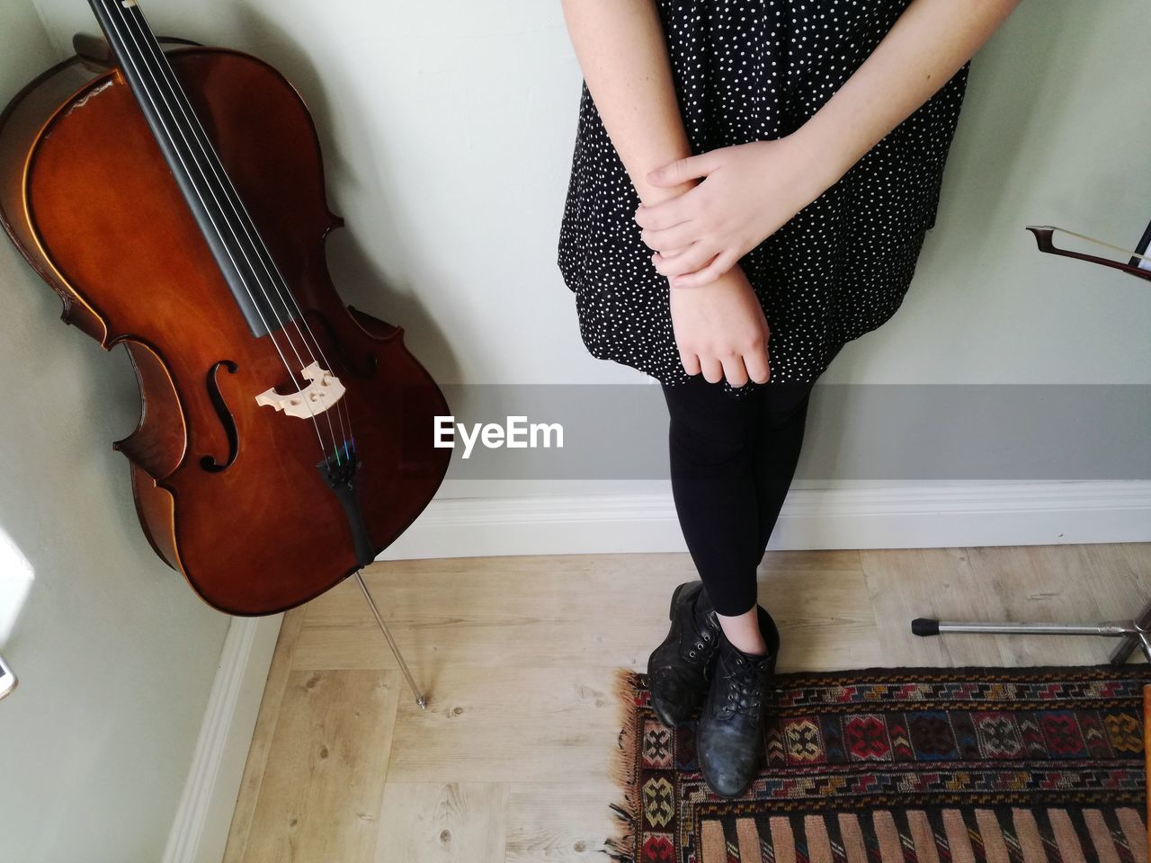 Low section of woman standing by cello against wall