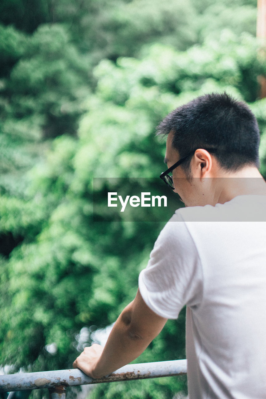 Rear view of man standing by railing against trees