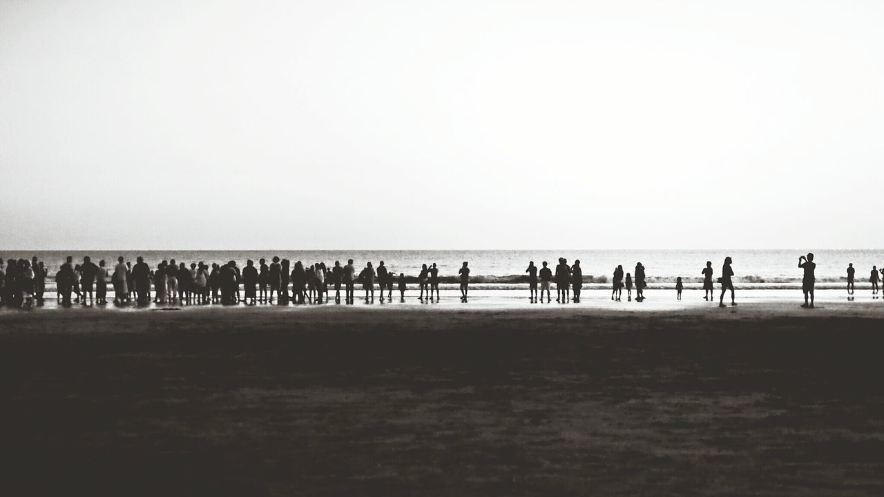 People on beach by sea against clear sky