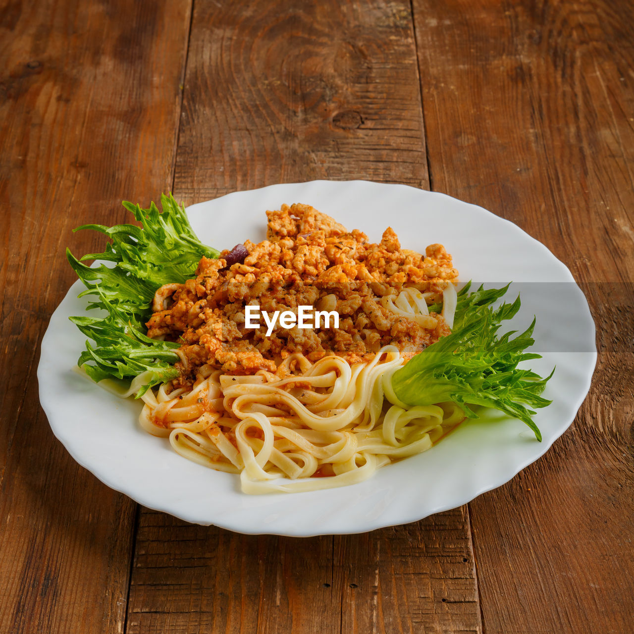 A plate of pasta in bolognese sauce on a wooden table. vertical photo