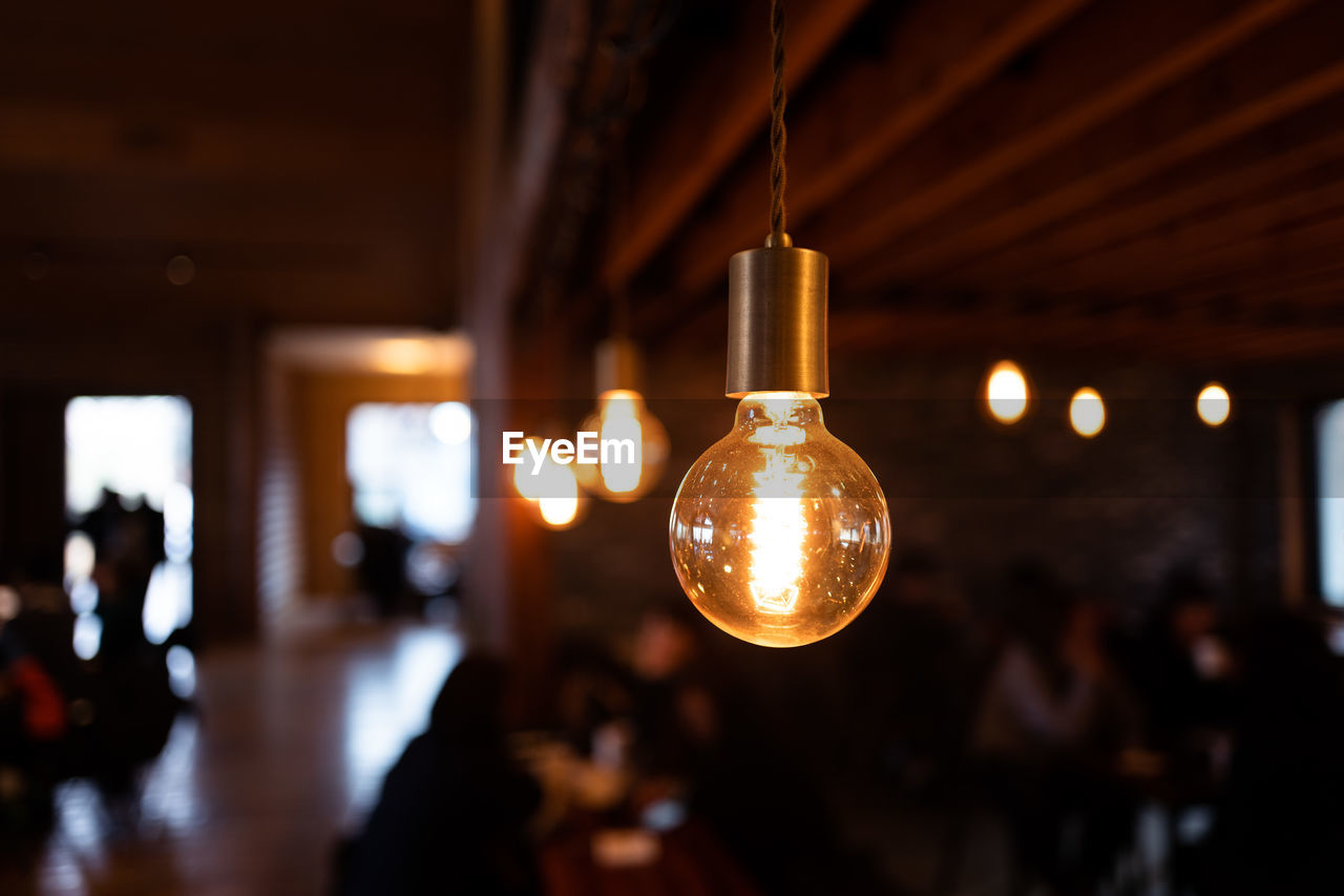 Close-up of illuminated light bulb hanging from ceiling in cafe