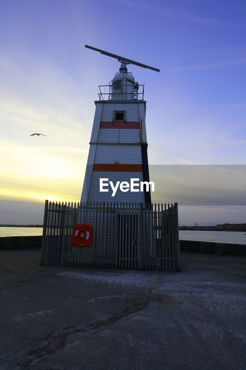 LIGHTHOUSE ON BEACH AGAINST SKY DURING SUNSET