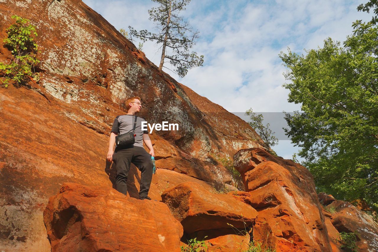 Low angle view of man on rock looking away against sky