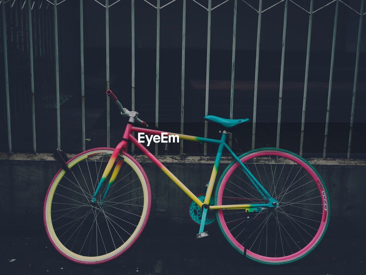 MULTI COLORED BICYCLE PARKED IN BASKET ON FENCE