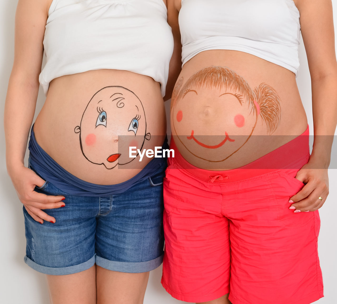 Midsection of pregnant women with painting bellies standing against white background