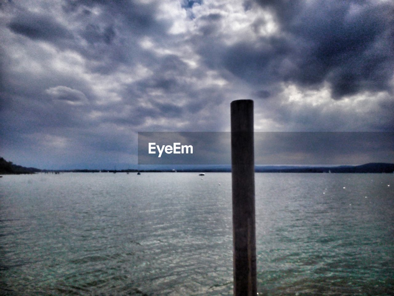 WOODEN POSTS IN SEA AGAINST CLOUDY SKY