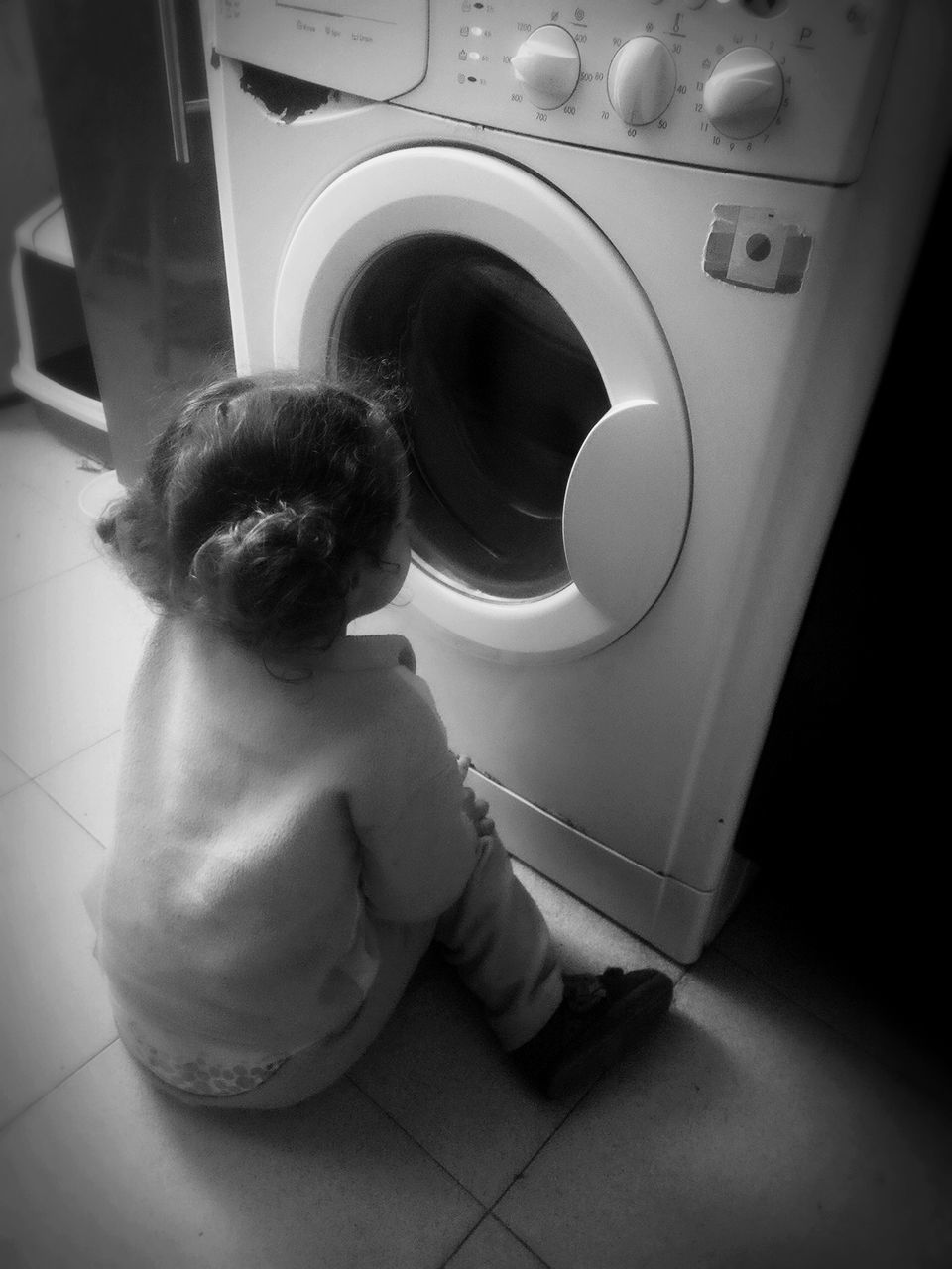 High angle view of baby girl sitting in front of washing machine at home