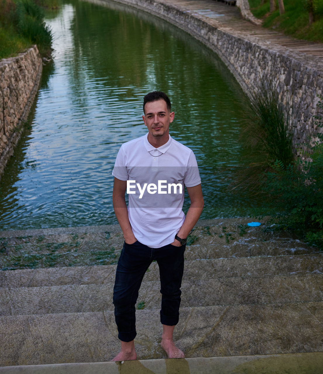 A young man in a white t-shirt posing inside a canal.