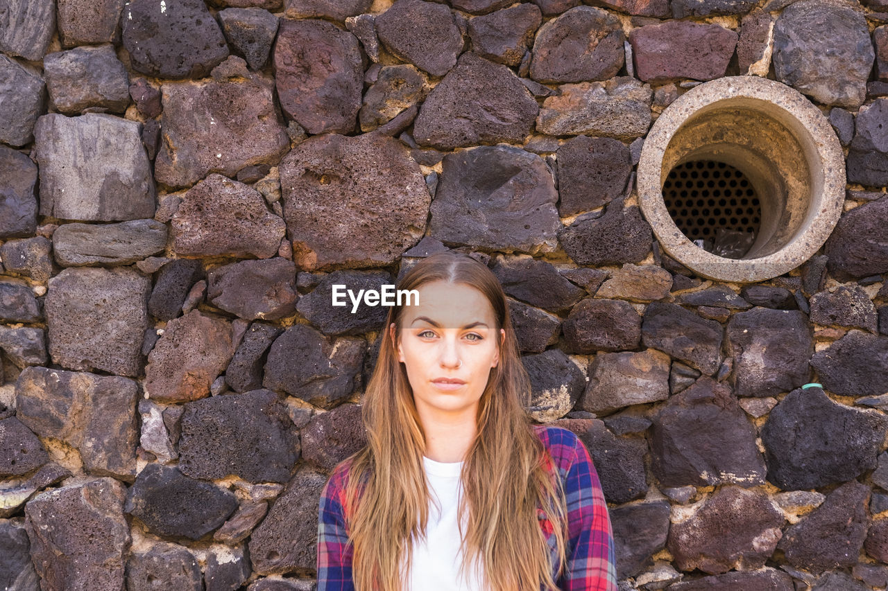 Portrait of young woman standing against stone wall