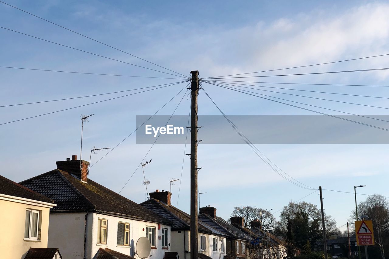 LOW ANGLE VIEW OF HOUSES AND ELECTRICITY PYLON AGAINST SKY