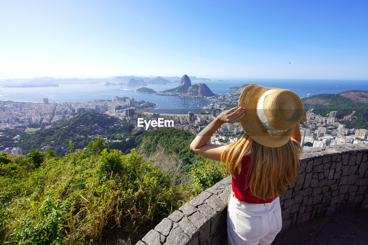 Stylish girl holding hat on rio de janeiro viewpoint with guanabara bay, rio de janeiro, brazil