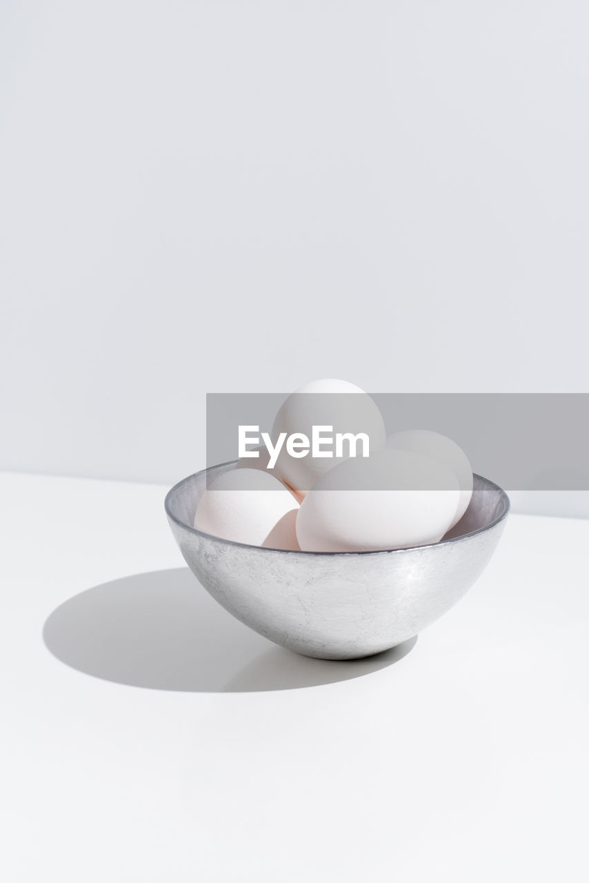 Bowl with fresh chicken eggs placed on table on white background in studio