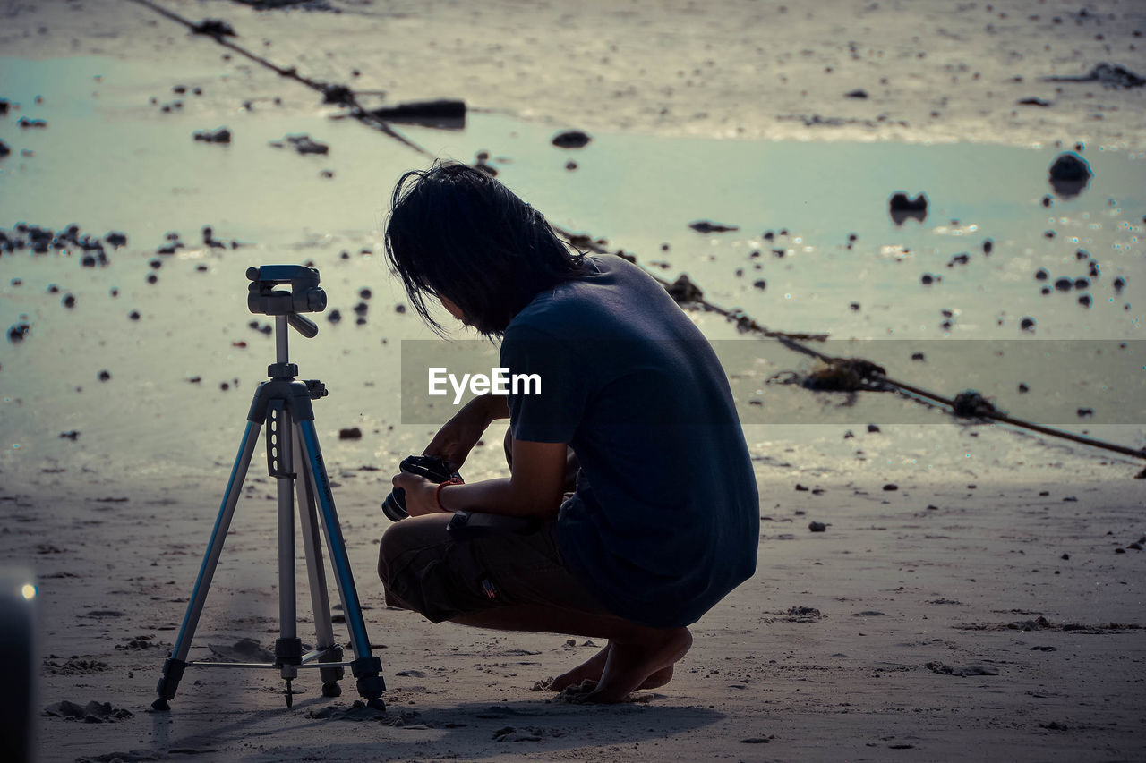 REAR VIEW OF MAN PHOTOGRAPHING ON SHORE