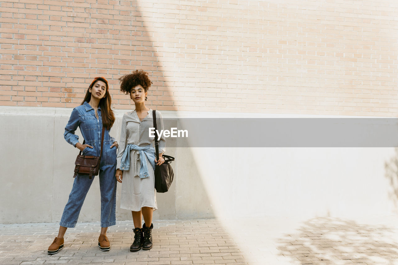 Women with bag standing against brick wall