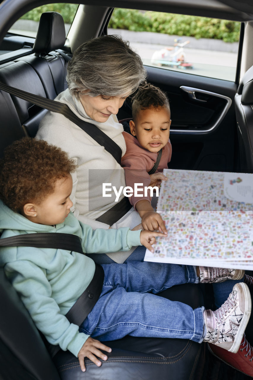 Senior woman reading book with children in car