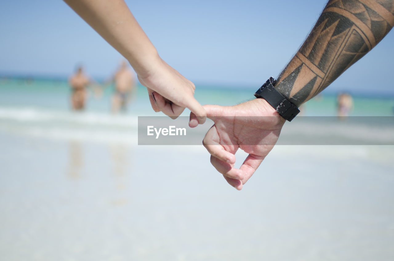 Cropped image of couple holding hands at beach