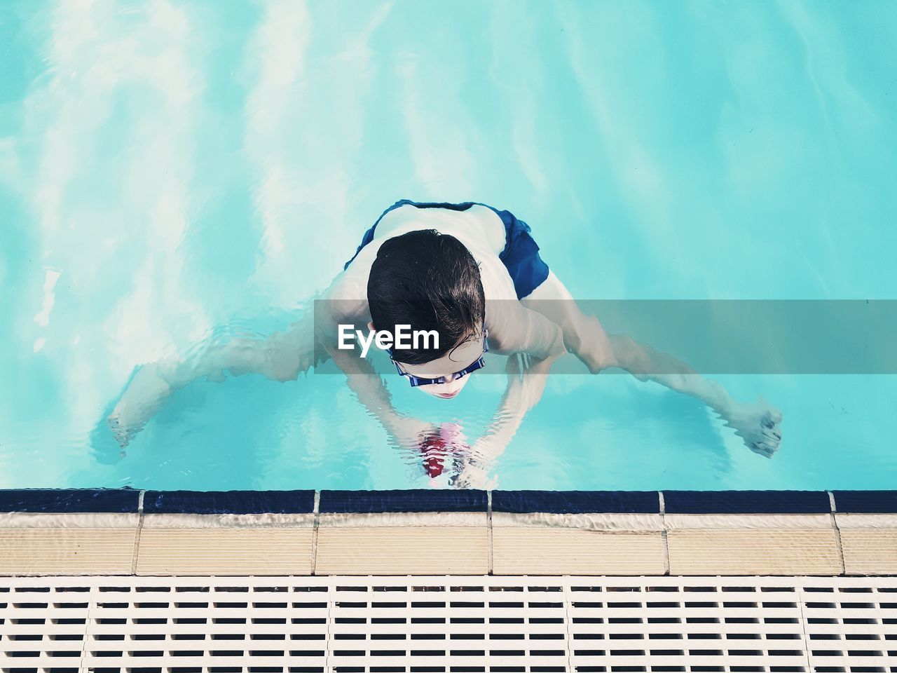 HIGH ANGLE VIEW OF YOUNG WOMAN SWIMMING IN POOL AT RESORT