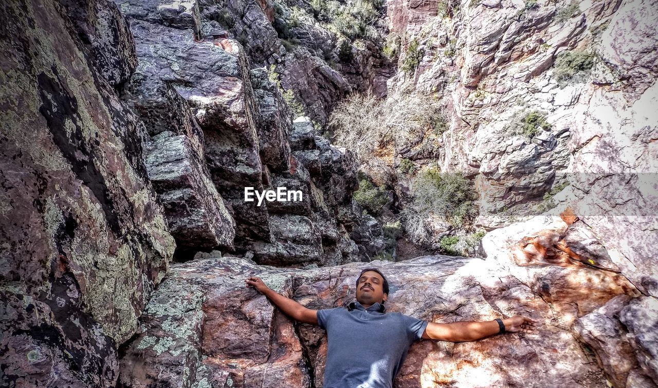 Man with arms outstretched leaning on rock