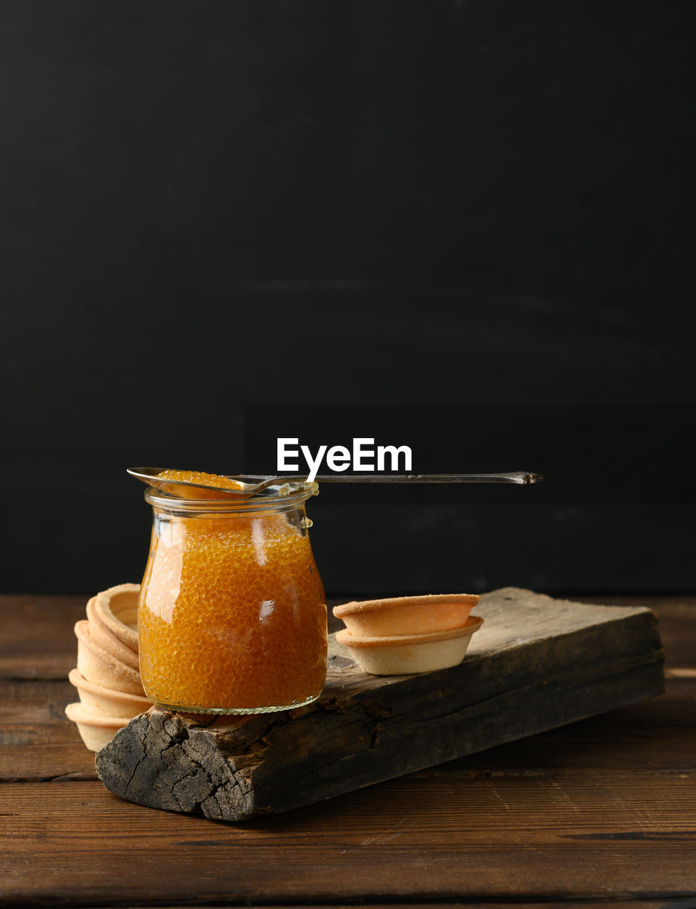 Pike caviar in a glass jar and round tartlets on a black background, close up, copy space