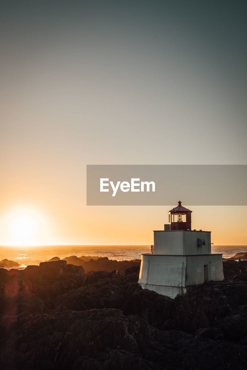 Lighthouse by sea against sky during sunset