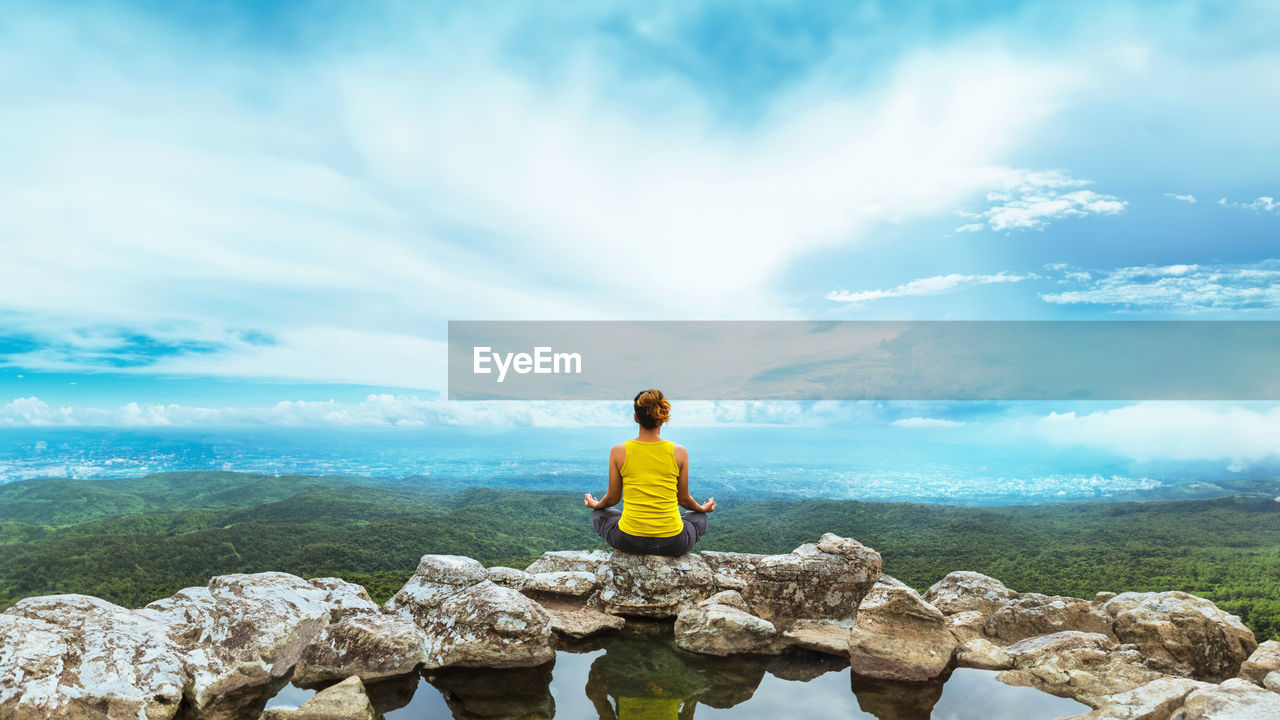 rear view of woman standing on rock against cloudy sky