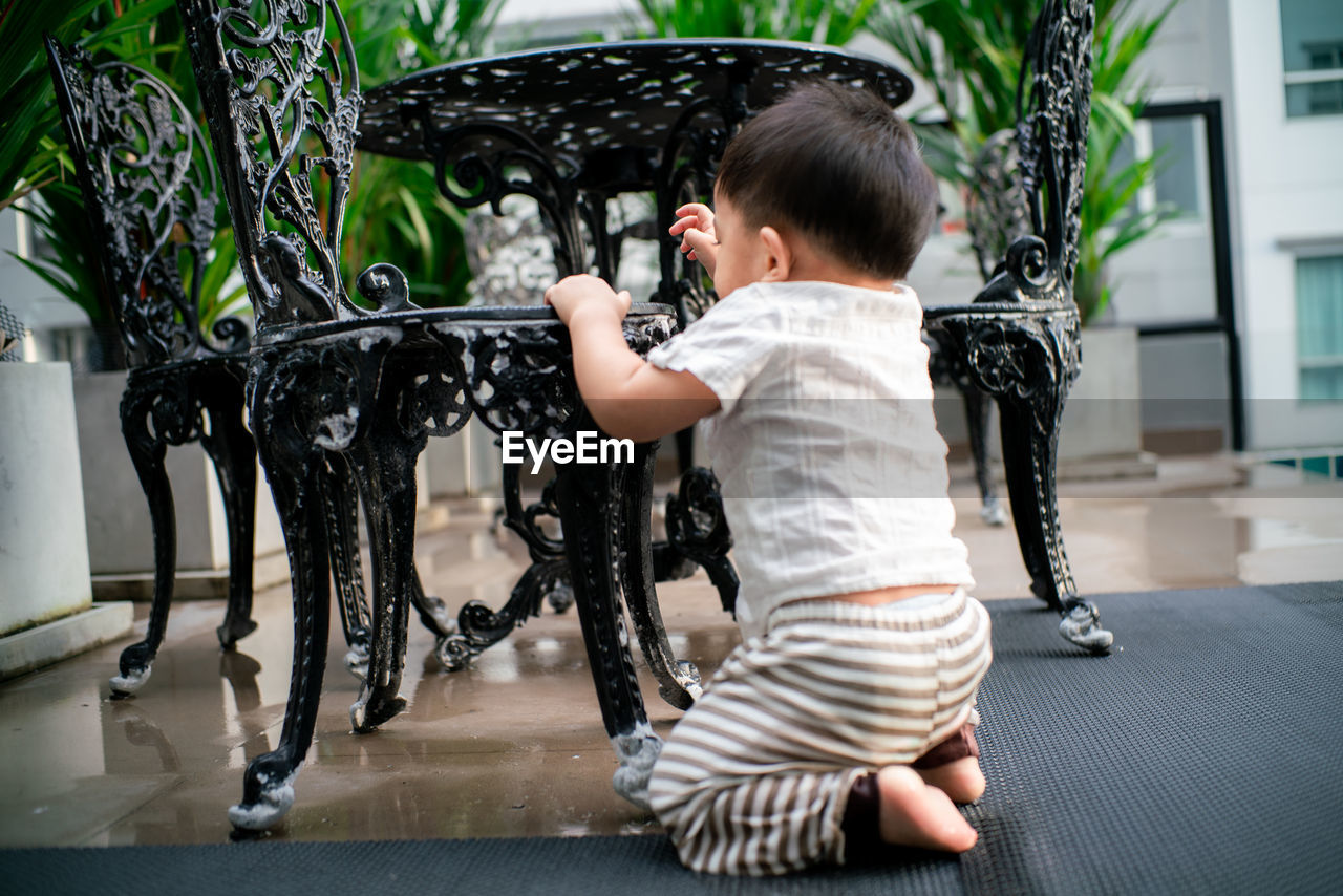 Cute boy crouching by chair outdoors