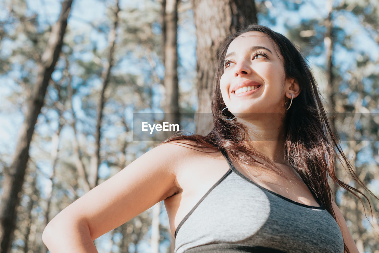 Portrait of young woman standing against trees