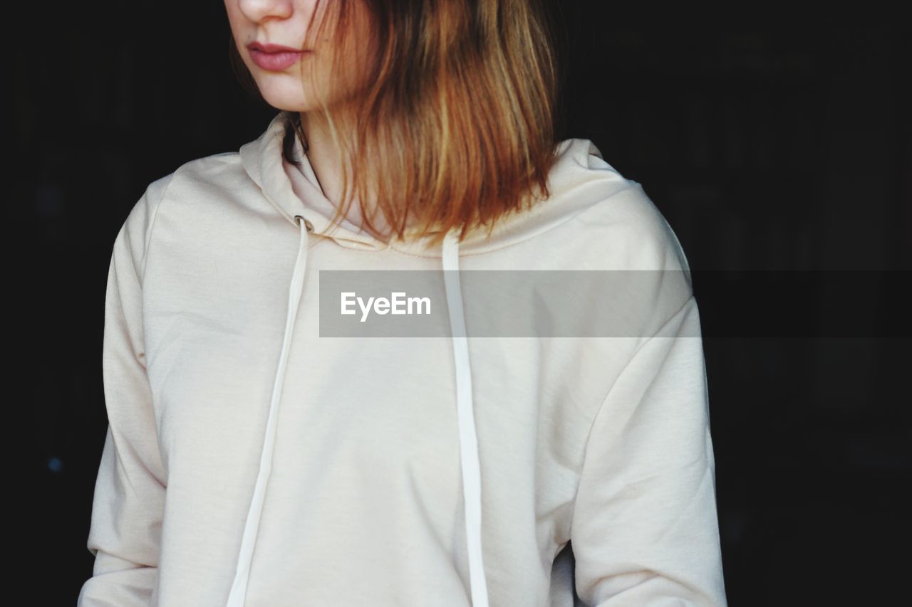 Midsection of woman wearing white hooded shirt against black background