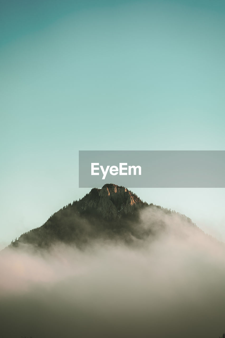 Scenic view of mountain amidst mist against clear sky