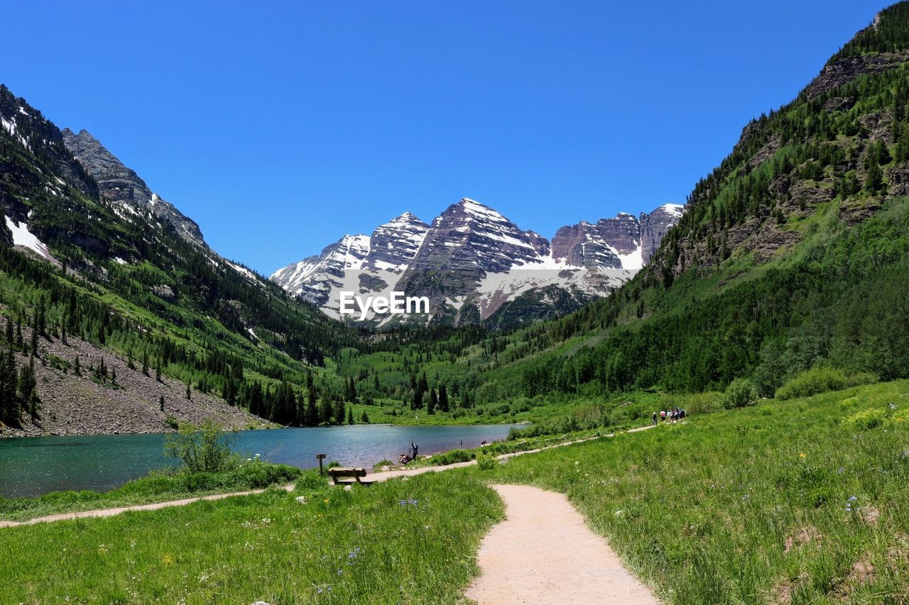 Pathway leading towards lake by maroon bells mountains against clear sky