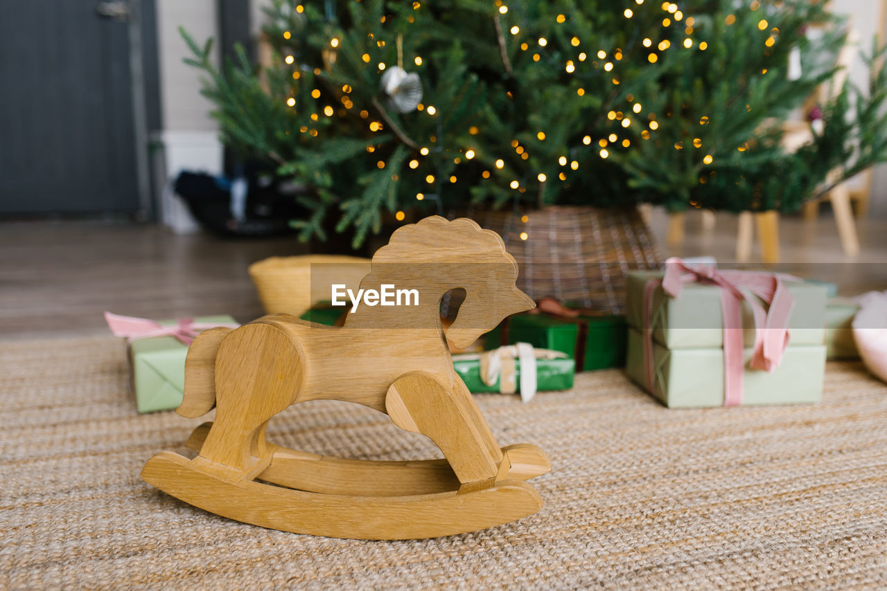 Wooden horse toy wheelchair on the background of christmas tree lights and gifts with copy space