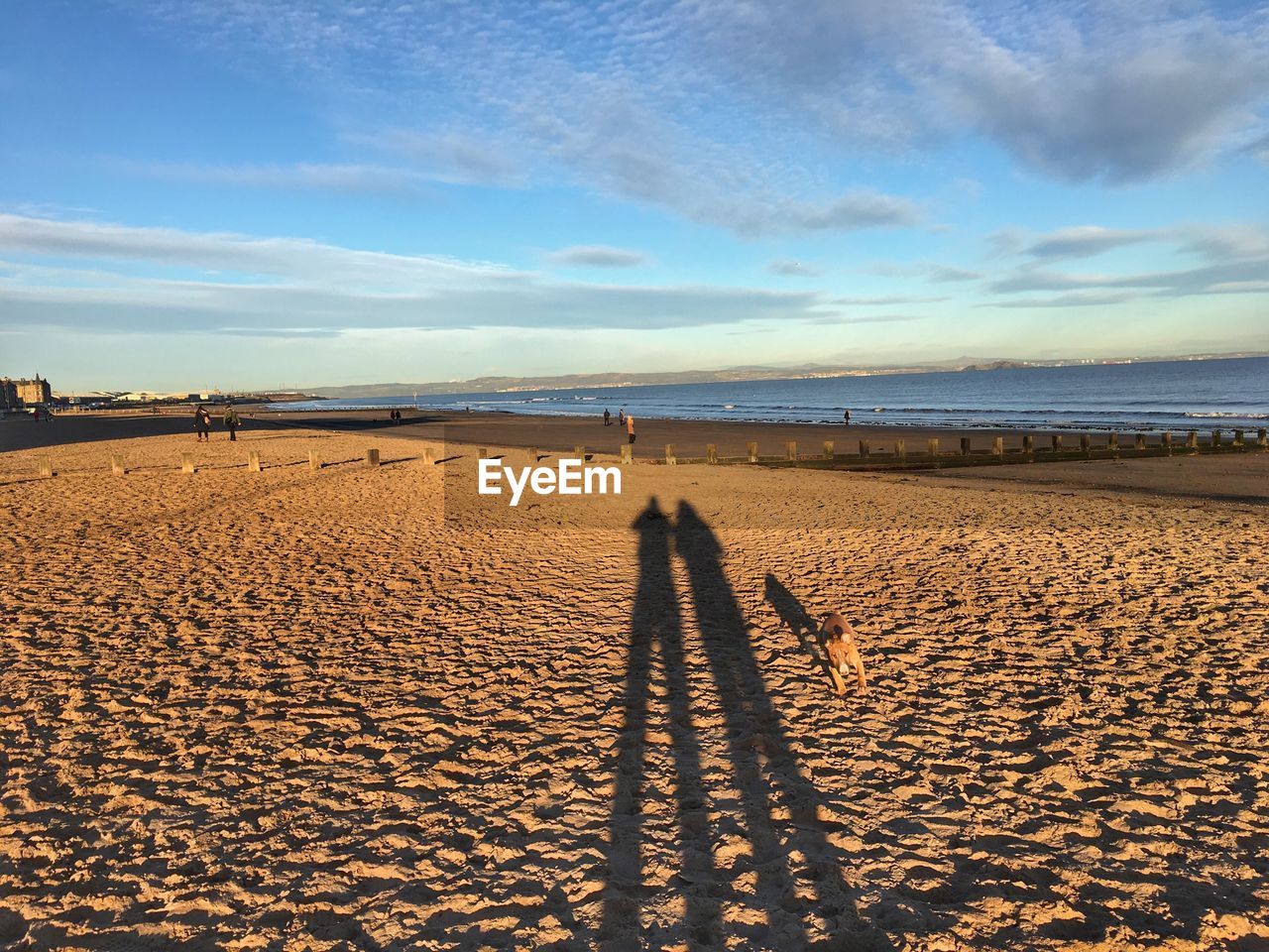 Shadow of people on sand at beach against sky