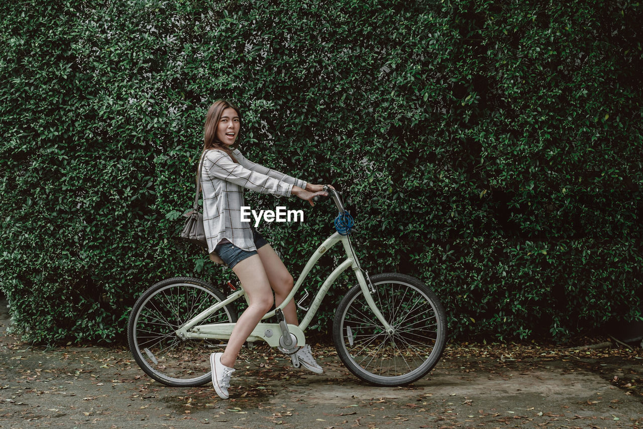 Full length portrait of woman riding bicycle against plants