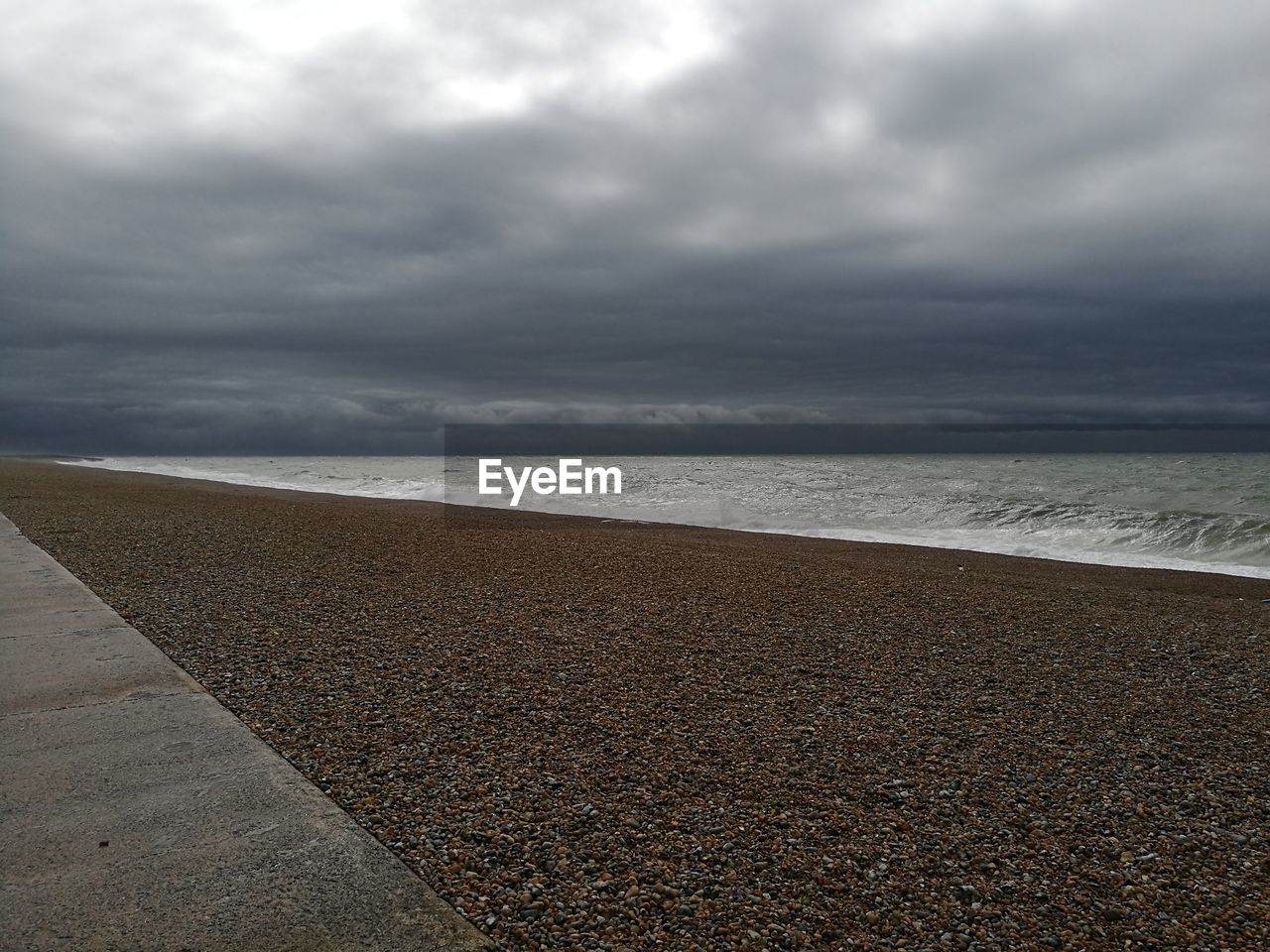 View of calm beach against cloudy sky