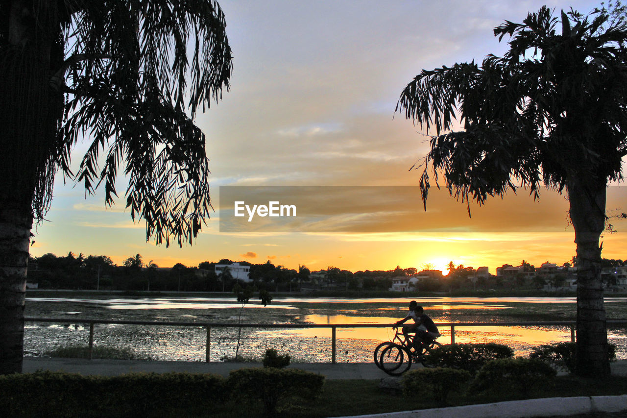 SILHOUETTE BICYCLE BY RIVER AGAINST SUNSET SKY