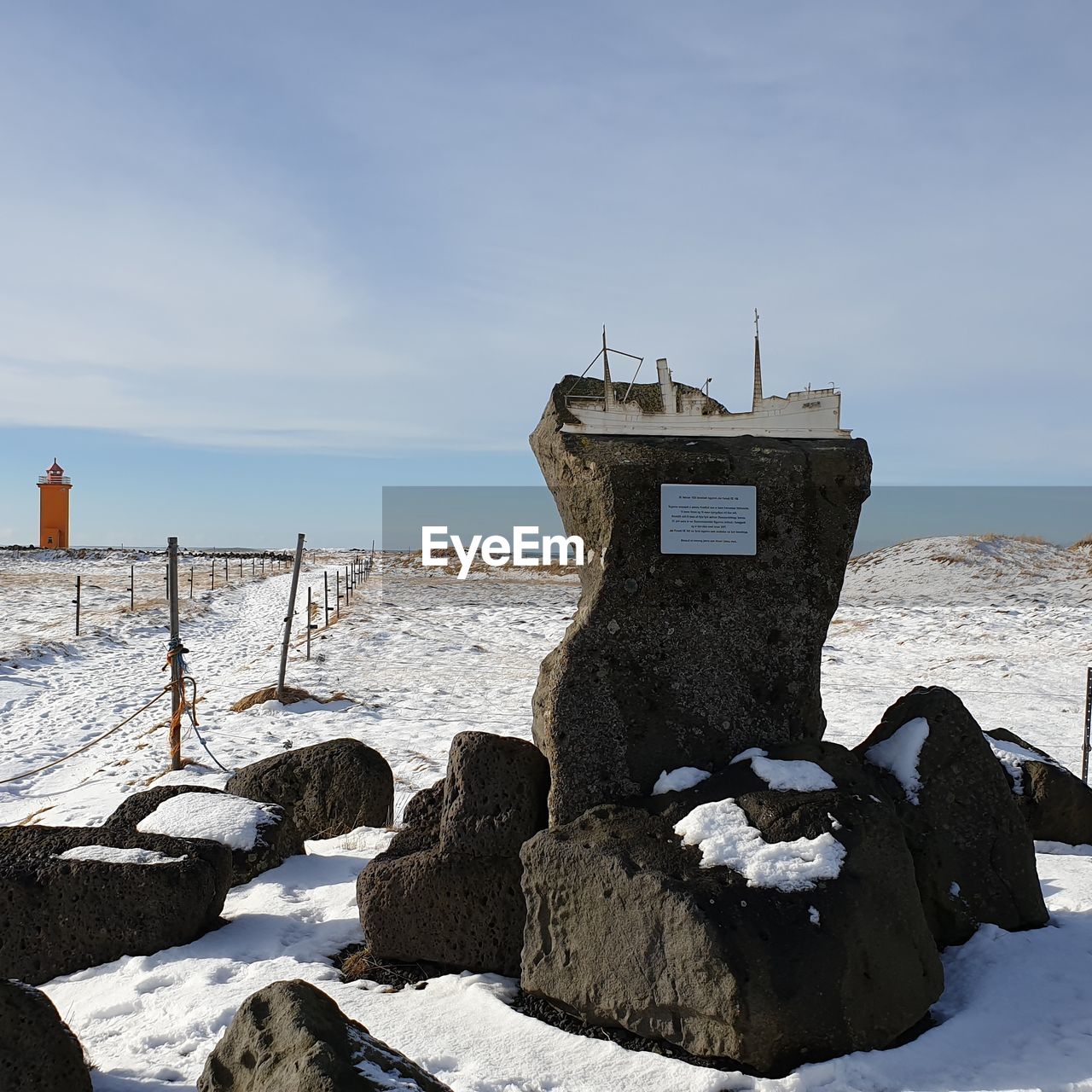 Cross on rock by sea against sky during winter