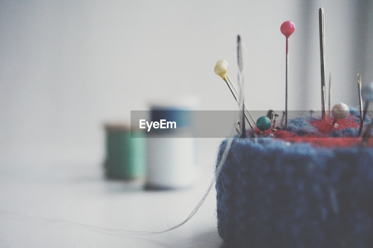 Close-up of sewing needle and thumbtacks on pin cushion over white background