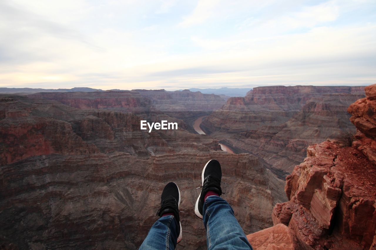 Low section of man on rock formation against sky