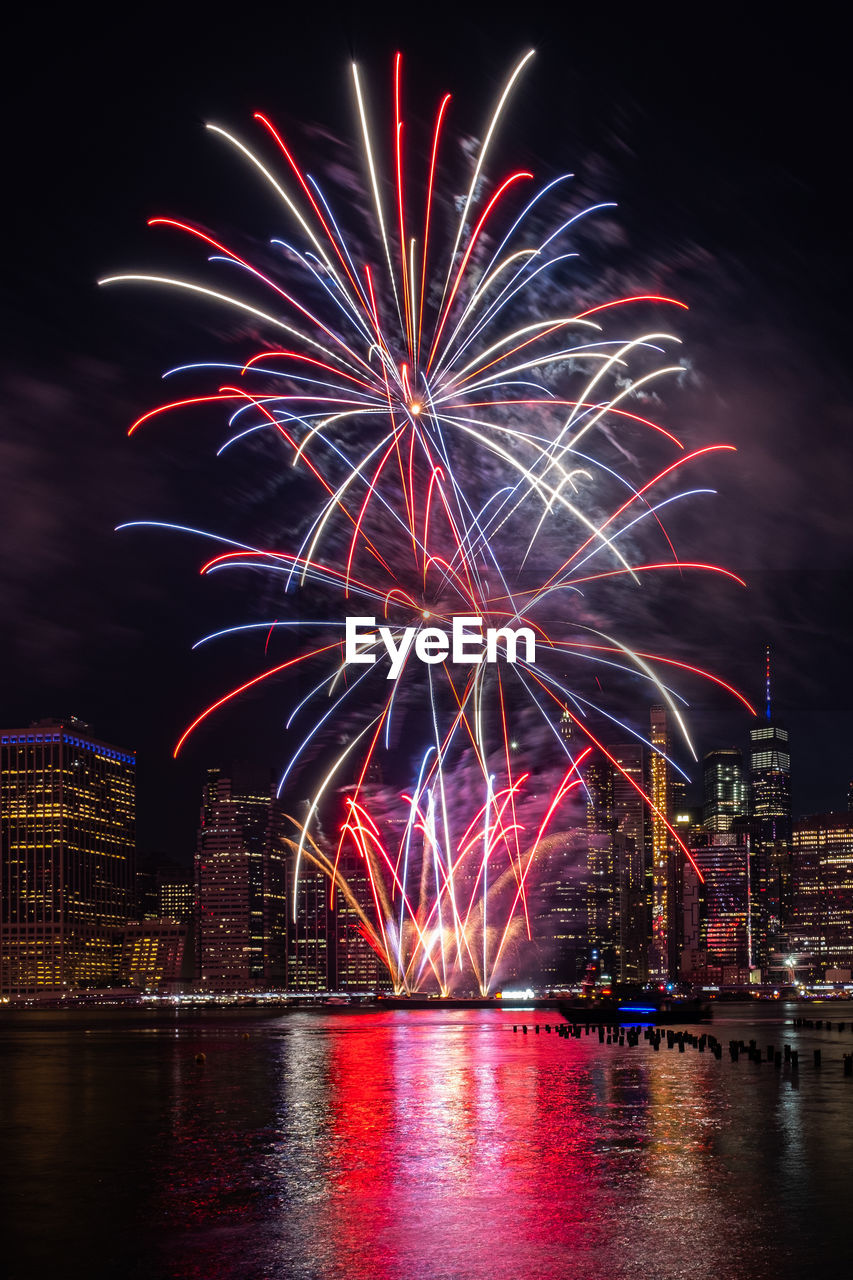 FIREWORK DISPLAY OVER ILLUMINATED CITY AGAINST SKY AT NIGHT