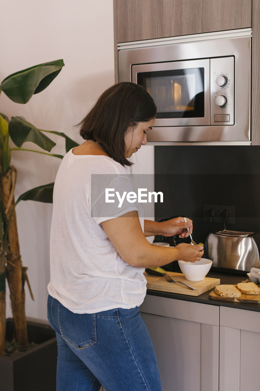 Concentrated woman preparing breakfast with avocados, eggs and bread