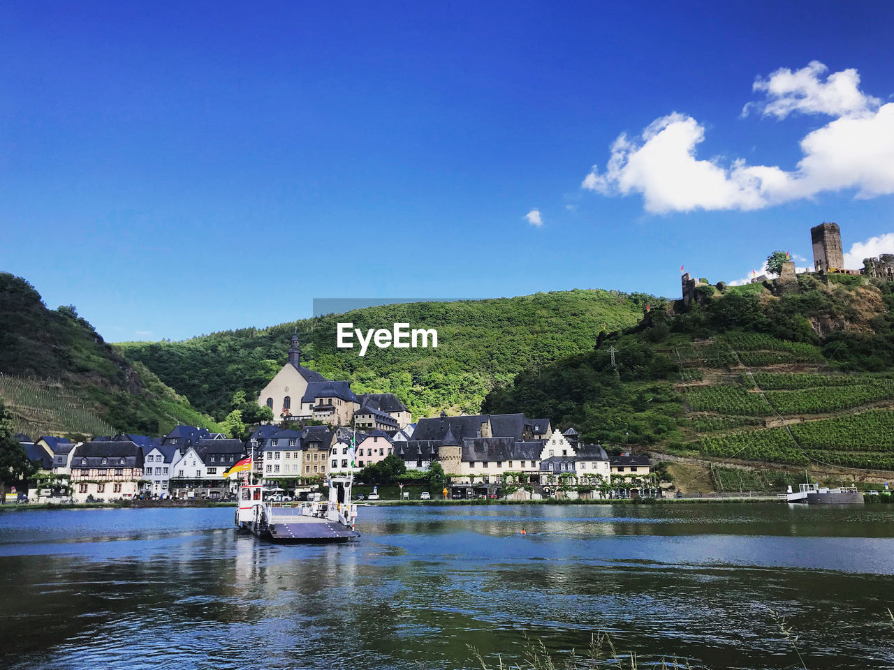 Houses by river moselle and buildings against blue sky