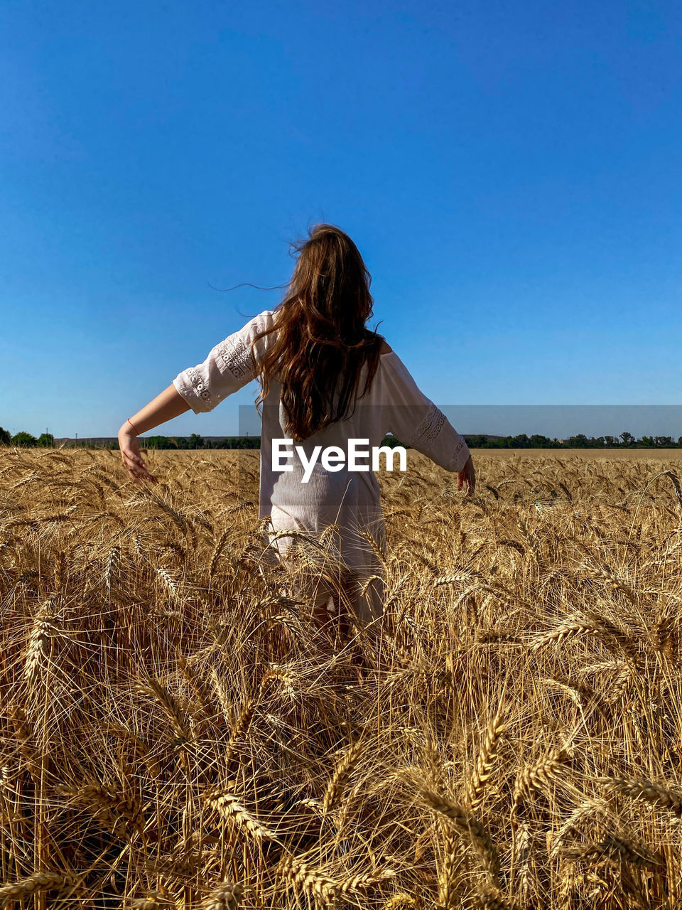 Rear view of woman standing on field against clear blue sky