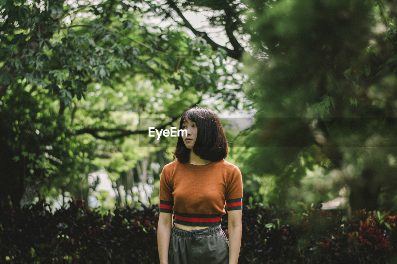 Thoughtful young woman looking away while standing against trees in park