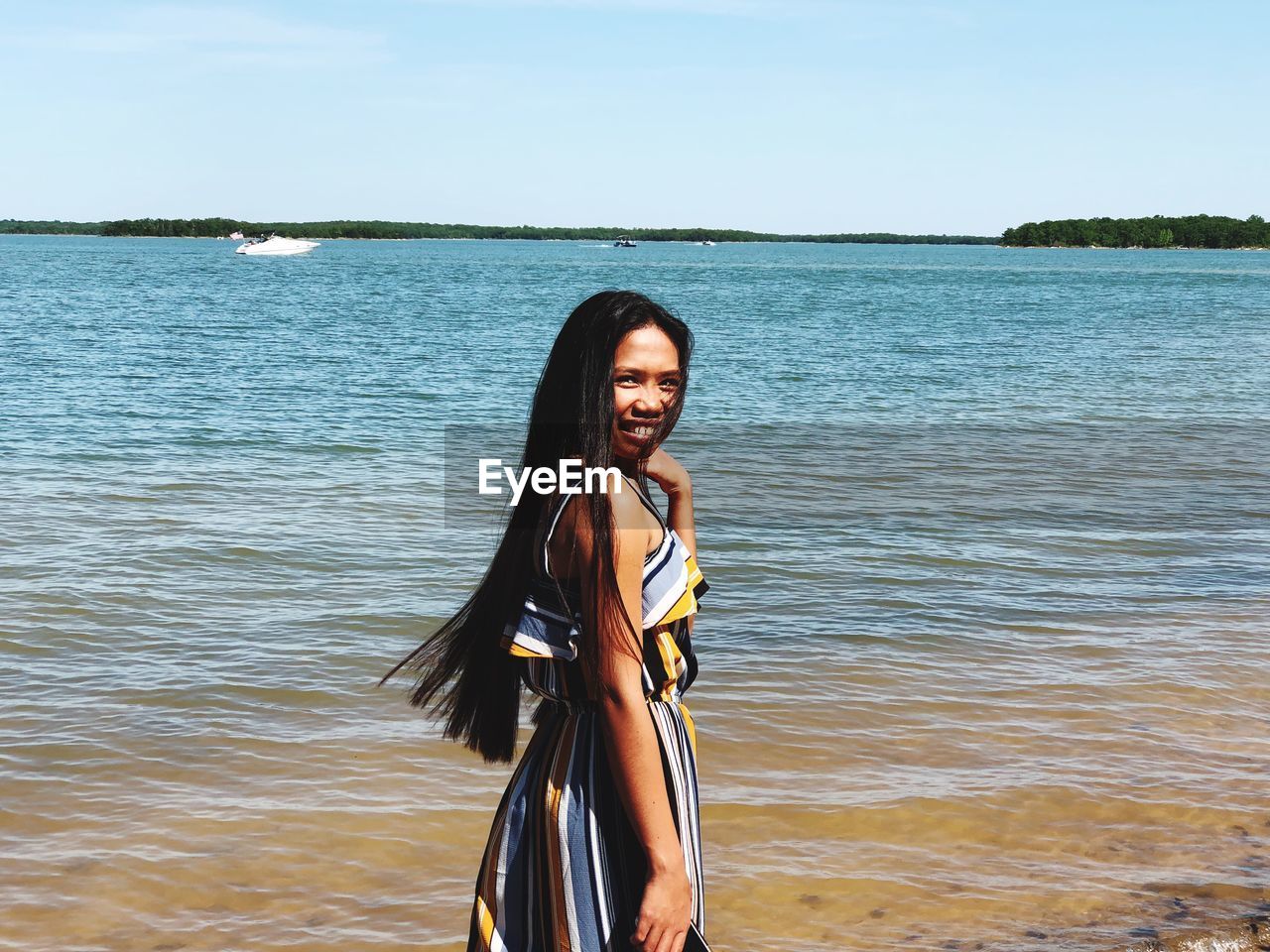 Portrait of young woman standing on shore at beach against sky