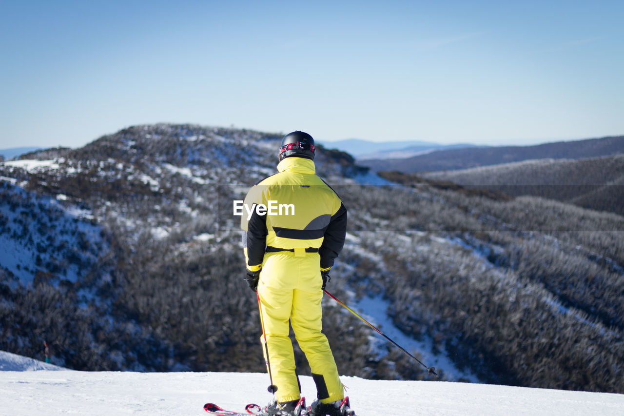 REAR VIEW OF MAN STANDING ON MOUNTAIN ROAD